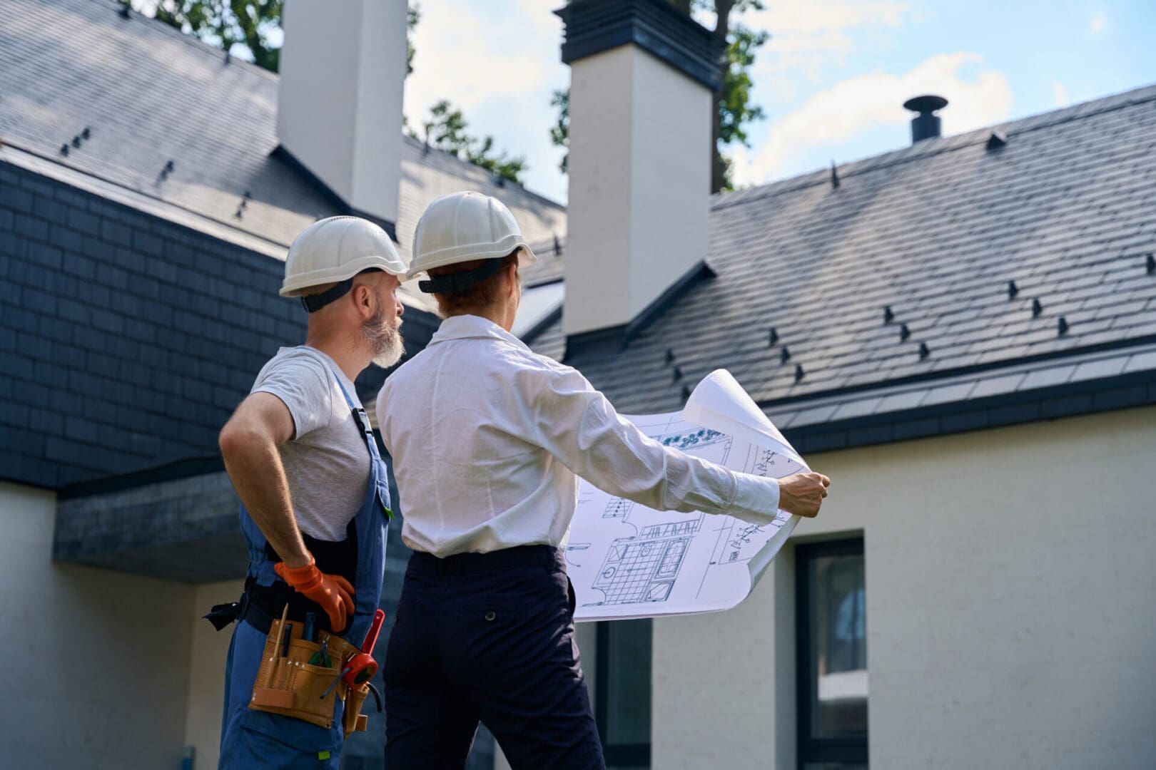 Architects reviewing building plans outside house.